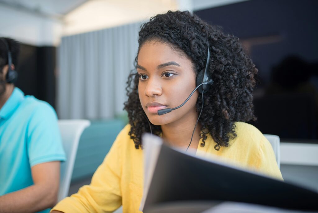 Building Efficient Support Teams Without Hiring In-House 1 A female customer support representative wearing a headset sits at her desk, looking intently at her computer screen.