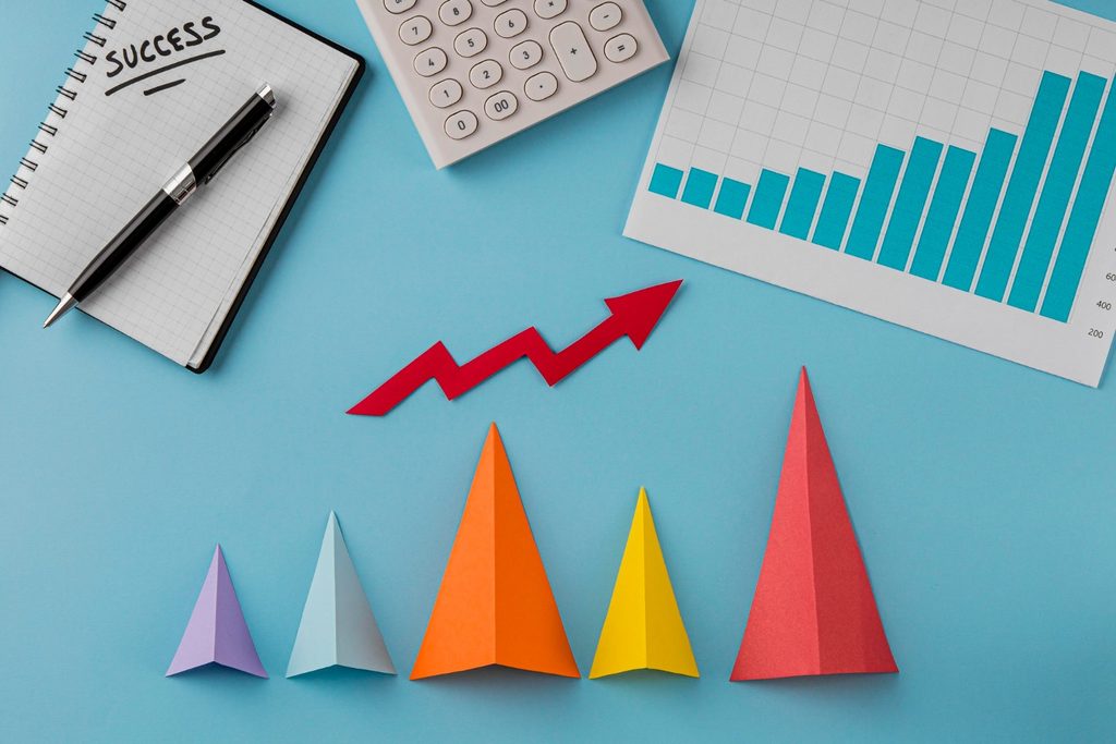 Why Hire a PR Agency? 5 Signs Your Brand Is Ready for Bigger Exposure 1 Top-down view of a business workspace with financial bar charts, a calculator, a notebook with the word success, and colorful paper pointers showing business growth.